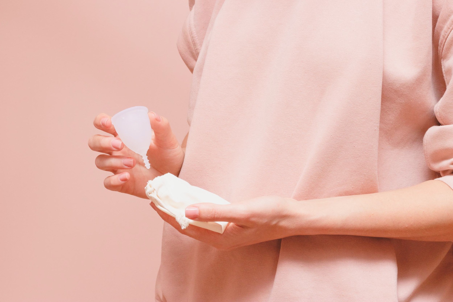 Hands holding a soft menstrual cup and its cotton pouch